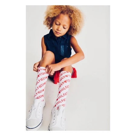 Child with curly blonde hair wearing a sleeveless dark blue top and printed white knee-high socks pulling up their socks