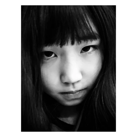 Black and white portrait of an Asian woman with dark hair and bangs, looking directly at the camera with a serious expression.