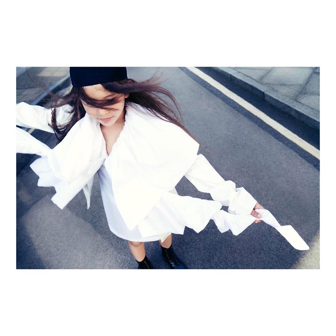 Young woman in a white dress and black hat stands outside on concrete with white accents, creating a modern, minimalist aesthetic.