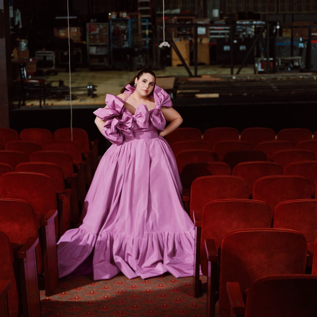 Woman in a lilac gown poses in a red-seated theater, creating a striking contrast between the dress and the vintage venue.