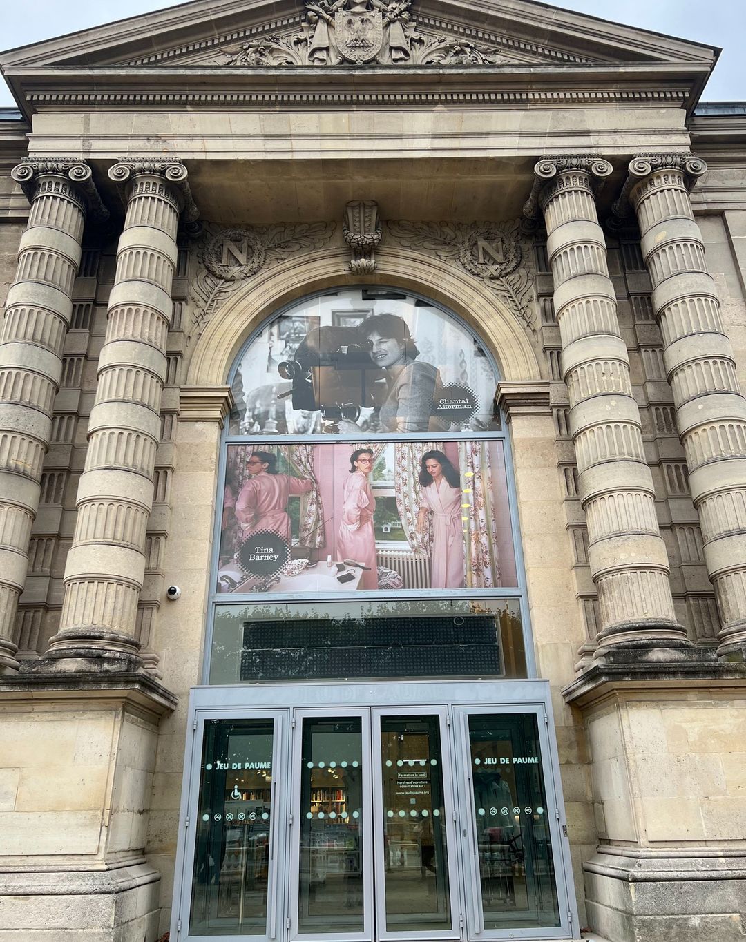 Exterior of Jeu de Paume in Paris featuring a large window with posters of women in pink robes and a vintage camera.