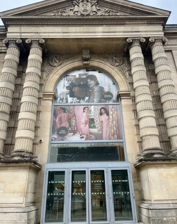 Exterior of Jeu de Paume in Paris featuring a large window with posters of women in pink robes and a vintage camera.