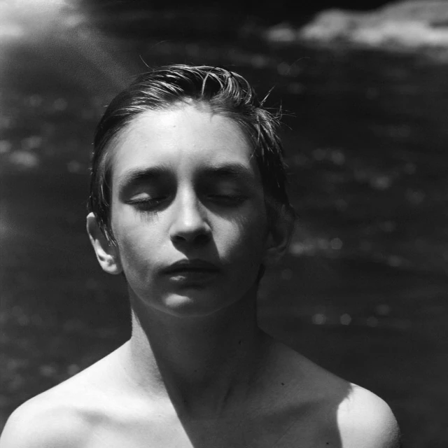 Monochrome portrait of a young person with closed eyes against a blurred dark background, bathed in soft, directional lighting.