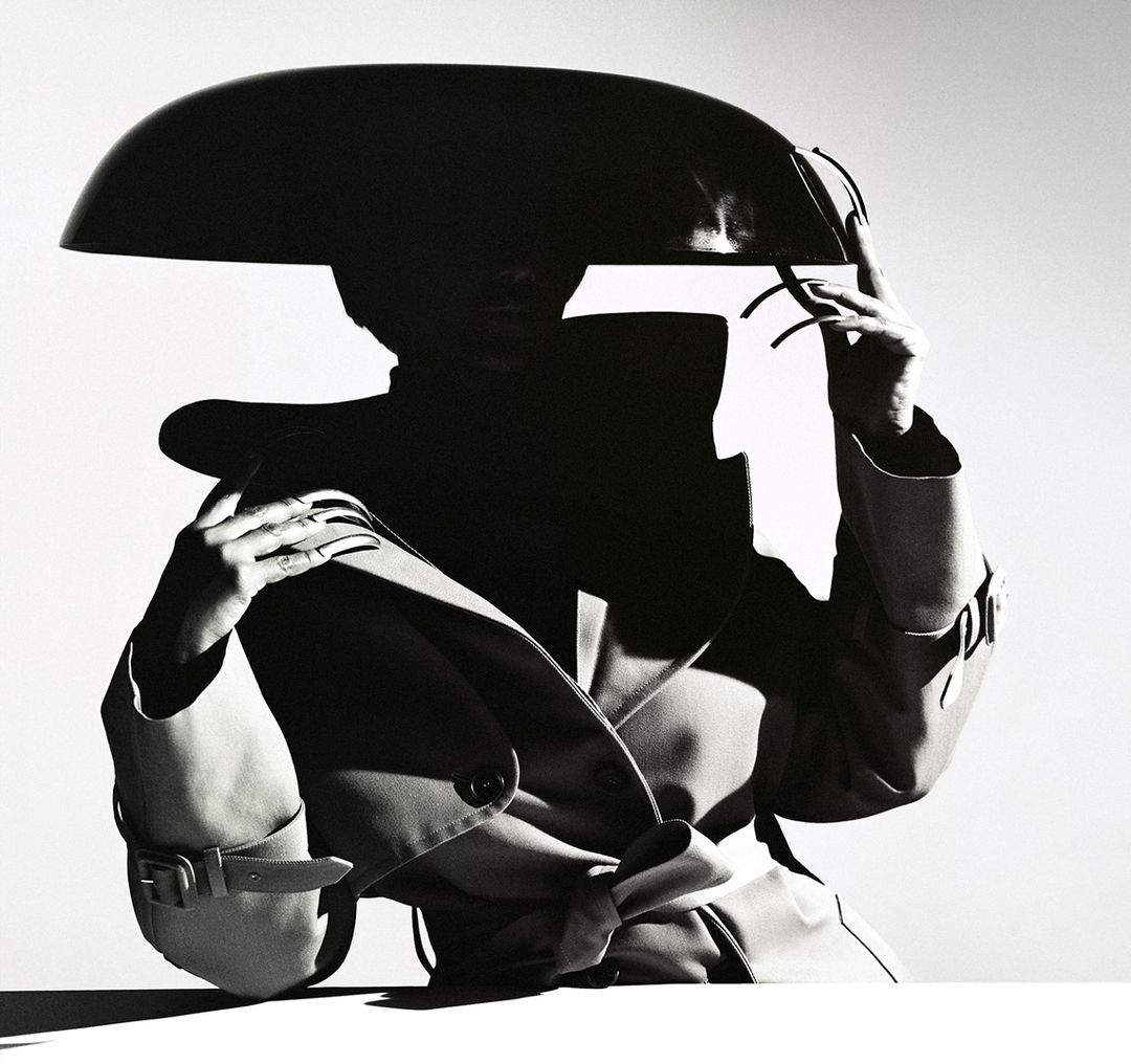 Model wearing a structured wide hat and belted trench coat against a white background by photographer Tina Tyrell.