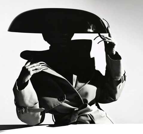 Model wearing a structured wide hat and belted trench coat against a white background by photographer Tina Tyrell.