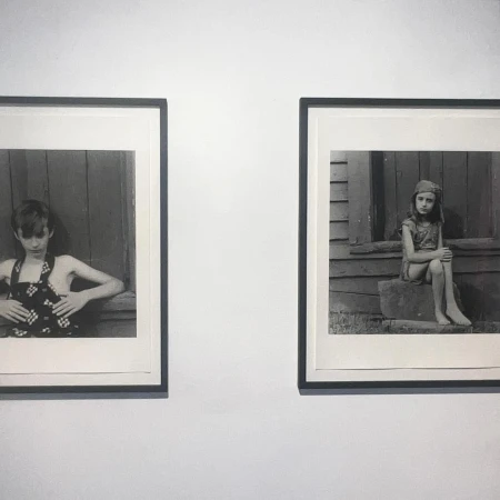 Two black and white photographs of children hang side-by-side on a white wall, each framed with a dark frame and a white matte.