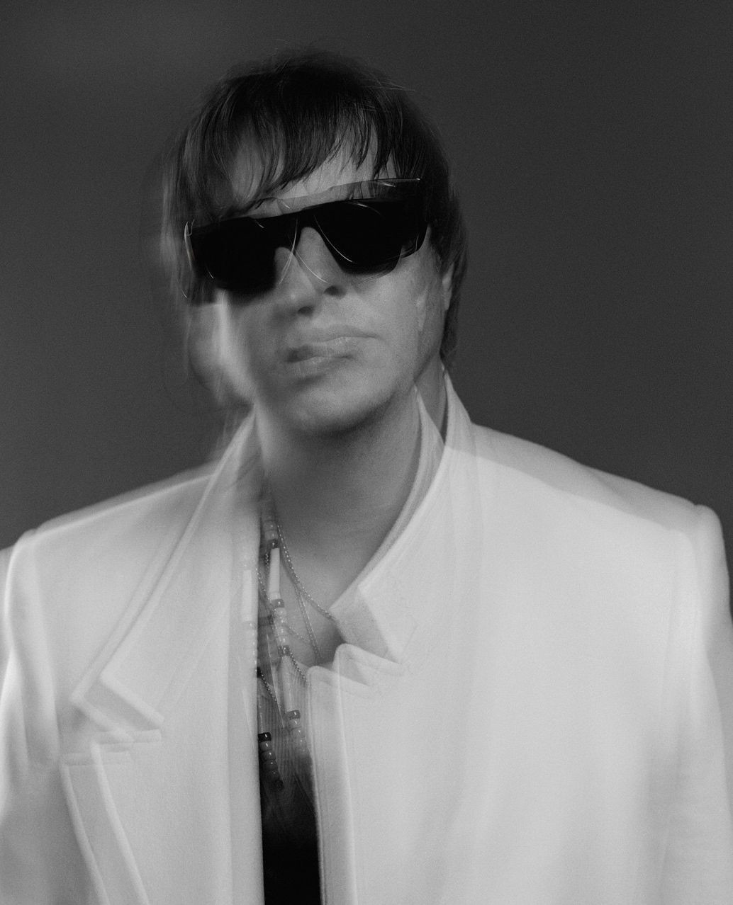 Portrait of a person wearing sunglasses and a white jacket with motion blur effect captured by Tina Tyrell