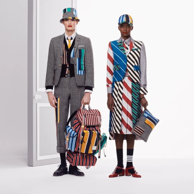 Two fashion models pose in matching, striped and plaid patterned outfits and bucket hats in a bright, minimalist studio environment.