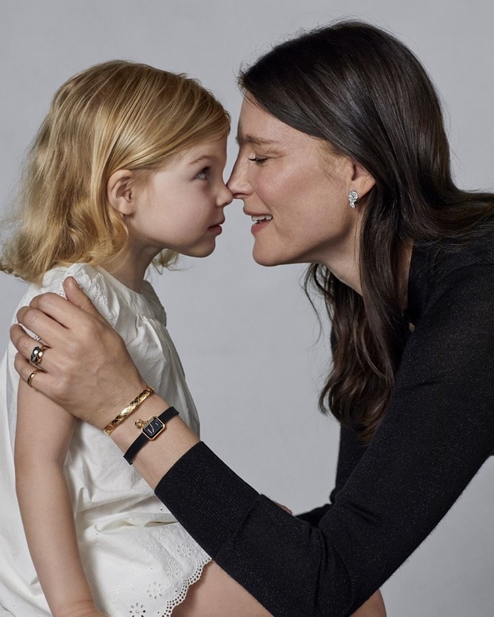 Close-up of a mother and daughter touching noses in a gentle, intimate moment, accessorized with rings, a bangle, and a classic wristwatch.