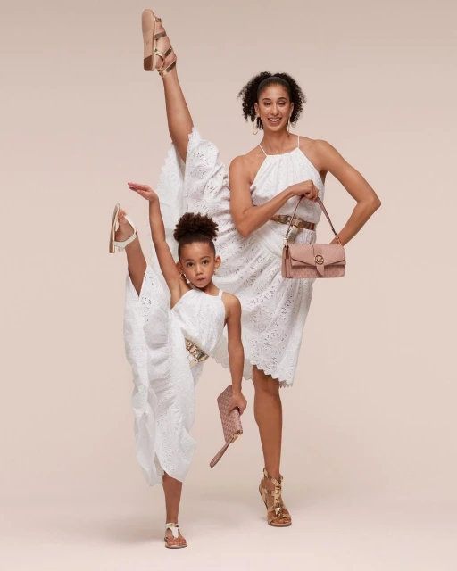 Fashion shot of an adult and child modeling dresses and accessories in a studio. Both are mid-pose in fashionable attire.