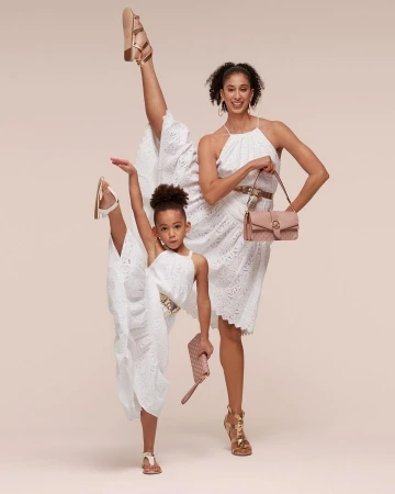 Fashion shot of an adult and child modeling dresses and accessories in a studio. Both are mid-pose in fashionable attire.