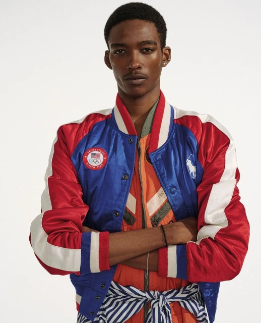 Adult male poses in a studio wearing a red, white, and blue Ralph Lauren Olympic bomber jacket with arms crossed in a medium shot.