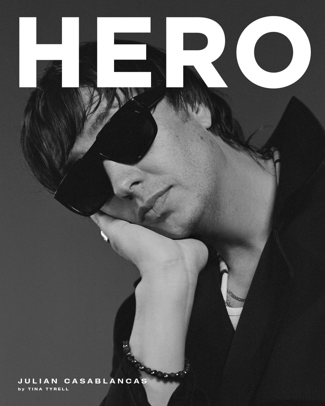 Black and white portrait of Julian Casablancas with sunglasses, resting his chin on his hand, alongside 'Hero' magazine text.