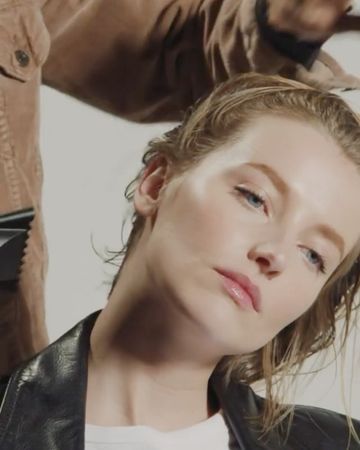 Close-up of a woman with blonde, wet hair and a black leather jacket, showcasing natural makeup in a photo studio environment.