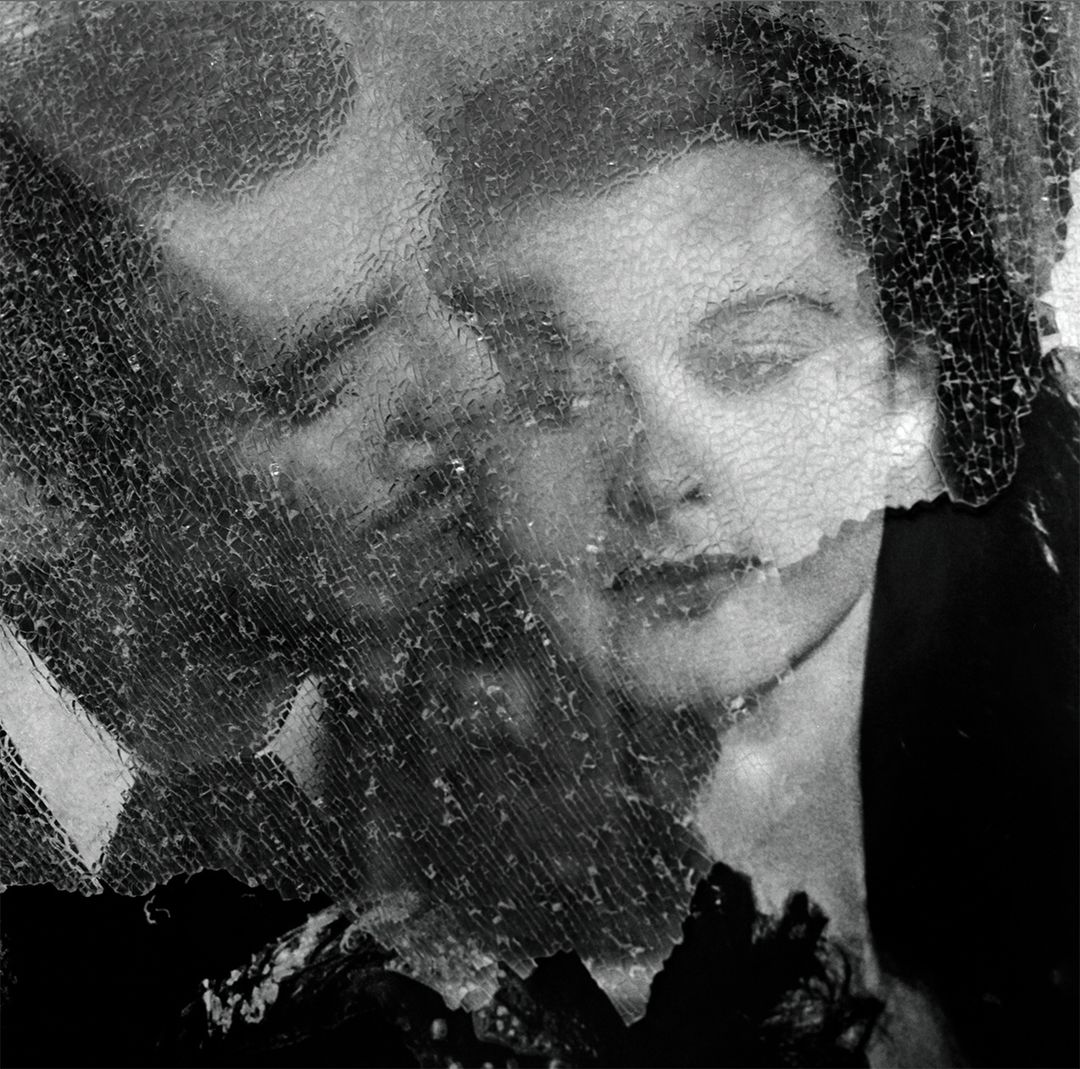 Monochrome image of a man and woman's faces behind a cracked glass surface, creating a distorted, artistic effect.
