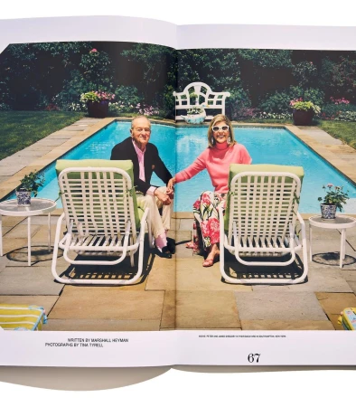 Couple seated in lawn chairs by a pool. The woman wears a pink sweater and floral pants, the man wears a blazer and pink shirt.