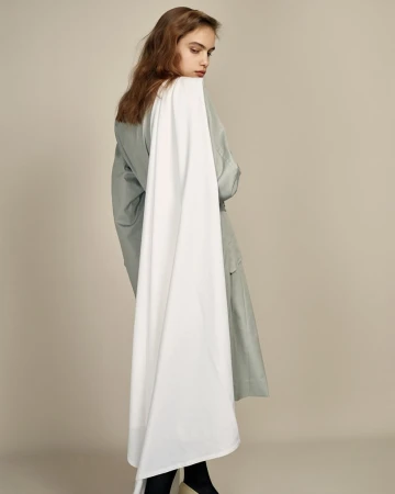 Model in sage green coat with a long white scarf draped over the shoulder against a neutral studio backdrop