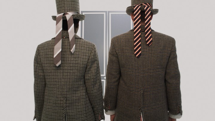 Two people stand with their backs to the viewer, wearing matching tweed suits, ties over their faces, and hats indoors.