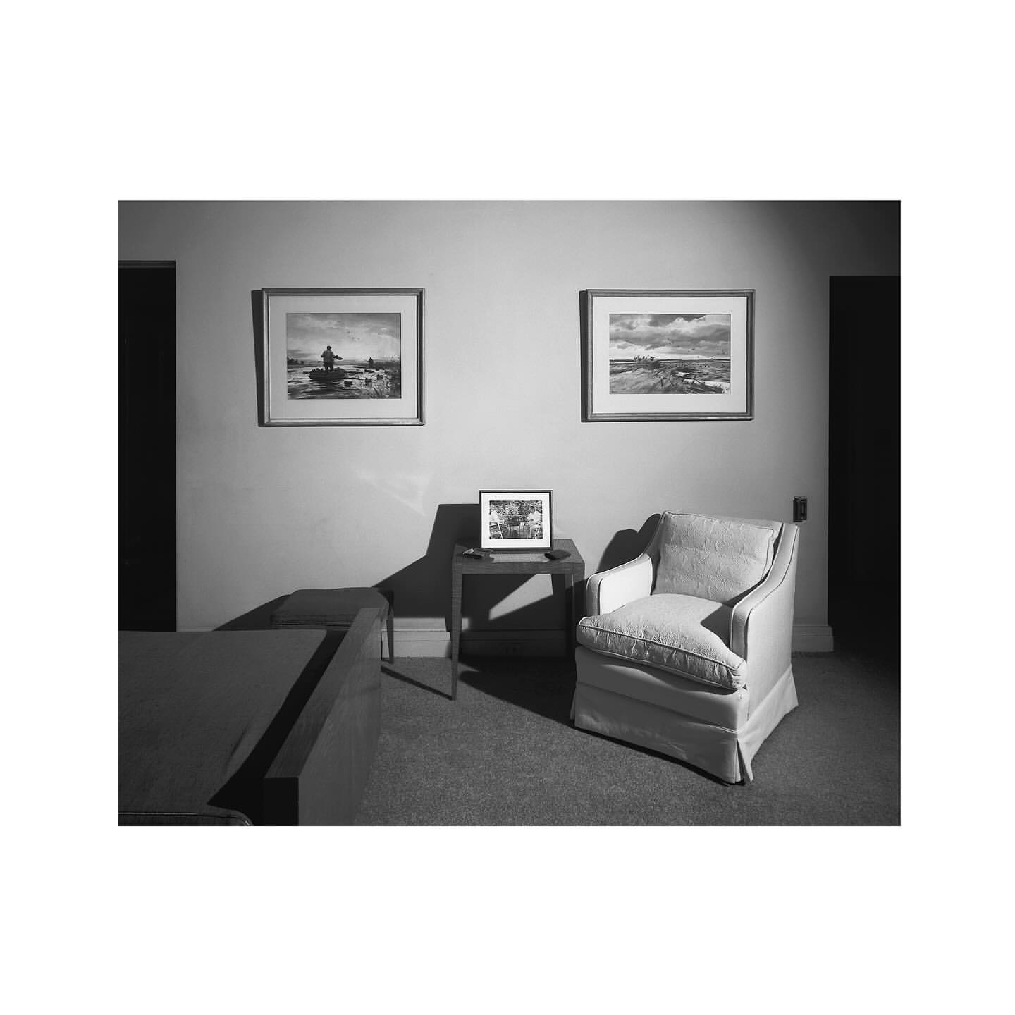 Monochromatic interior scene with chair, table, and framed artwork on a wall in front of carpet, evoking a calm and classic aesthetic.