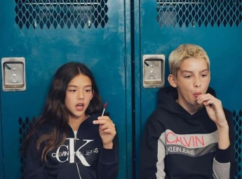 Two young models wearing branded hoodies eating lollipops in front of blue metal lockers captured by photographer Tina Tyrell.