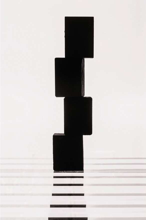 Abstract still life of a stack of four black cubes on a white surface with blurred horizontal black and grey lines, creating a minimalist design.
