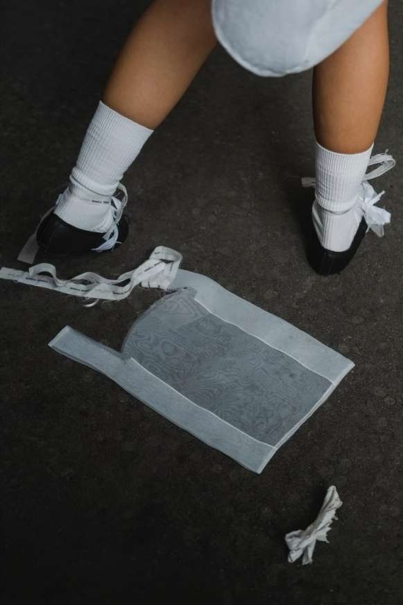Close-up of a child's legs, white socks, black tap shoes with white ribbons near discarded foot wraps on a dark grey surface.