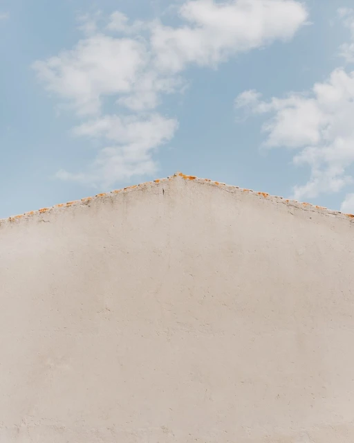 Abstract shot of a building facade with white stucco under a pale blue sky with scattered clouds in the background, daytime.