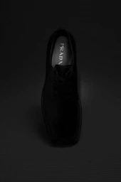 Overhead studio shot of a black leather dress shoe on a dark textured background with visible PRADA branding on the insole