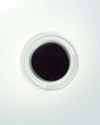 Top-down flat lay view of a white ceramic jar containing a dark purple cosmetic cream against a clean white background.