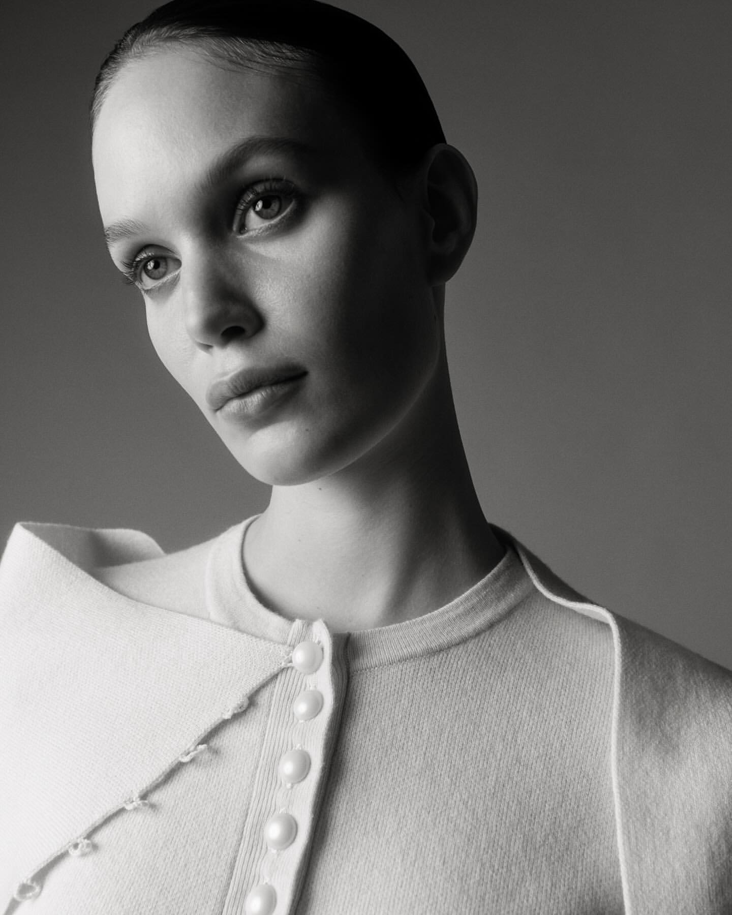 Monochromatic portrait of a young woman with short slicked-back hair wearing a white sweater, captured in a photo studio setting.