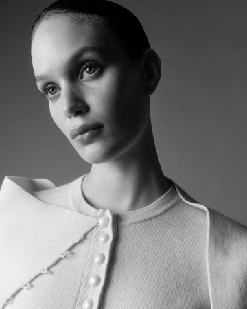 Monochromatic portrait of a young woman with short slicked-back hair wearing a white sweater, captured in a photo studio setting.