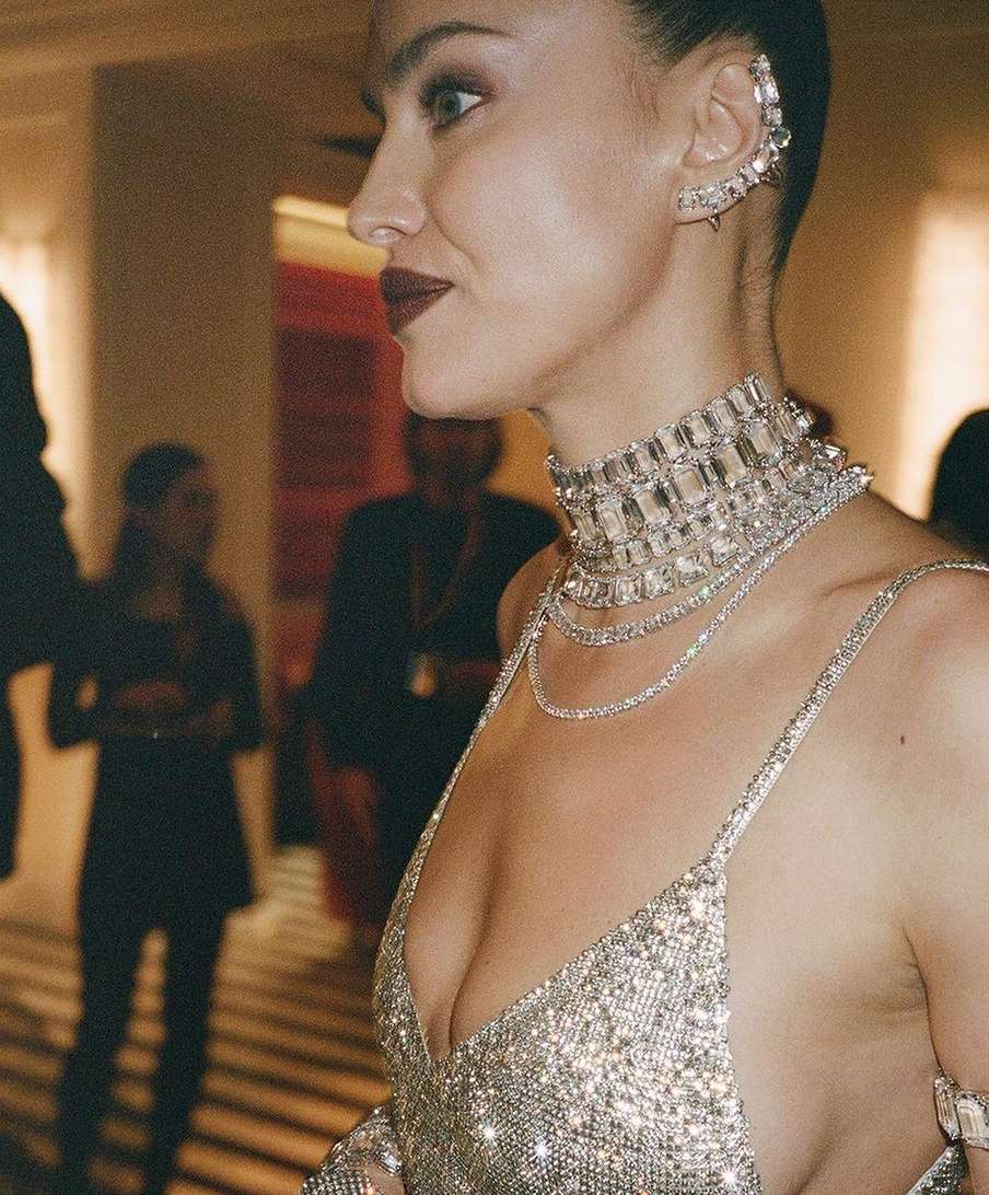 Profile shot of a woman wearing a sparkly silver dress and multiple pieces of sparkling jewelry in an indoor setting.