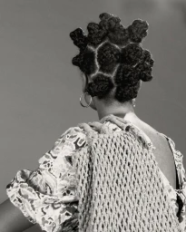 Monochrome portrait from behind of a black woman wearing patterned top and macrame bag with bantu knots hairstyle by Tobias Lundkvist.