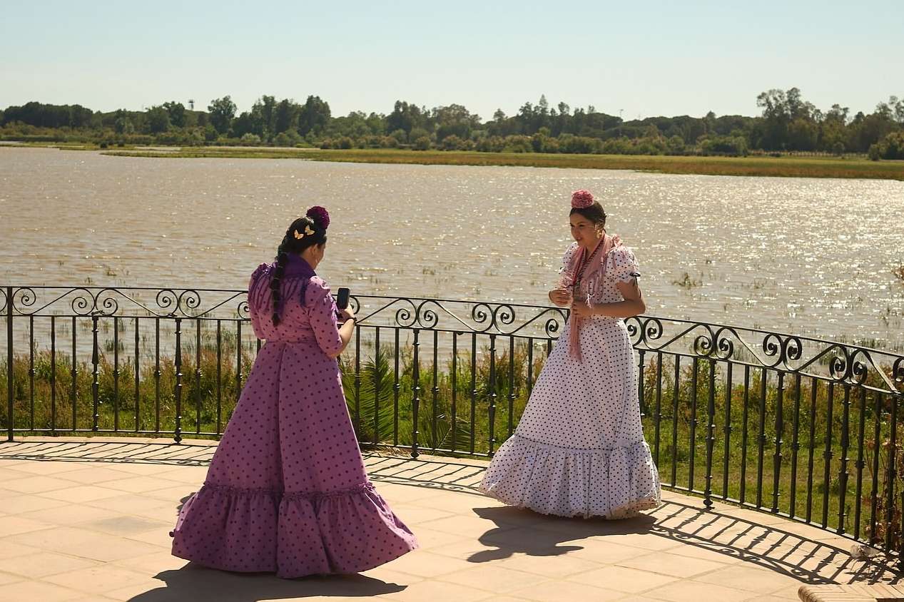 Two adult females in polka dot flamenco dresses pose near a railing overlooking a lake in an outdoor environment on a sunny day.
