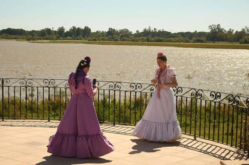Two adult females in polka dot flamenco dresses pose near a railing overlooking a lake in an outdoor environment on a sunny day.