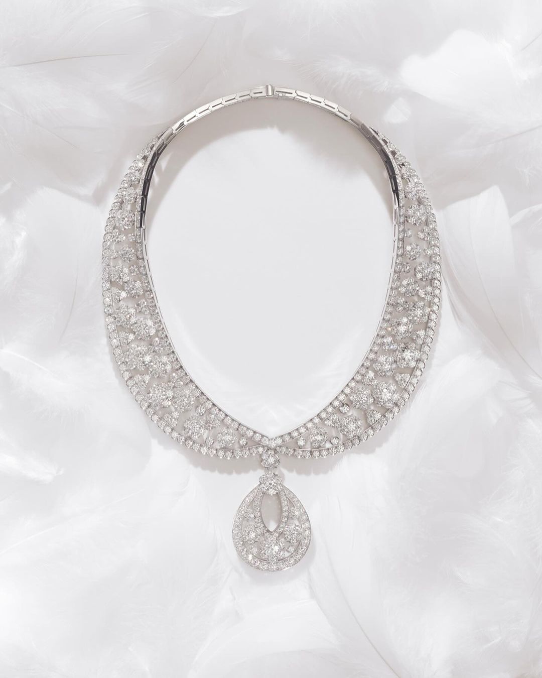 Elegant diamond necklace featuring a teardrop pendant, displayed on a soft white feathered surface, highlighting its intricate design and sparkle.