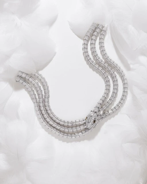 Serpentine diamond necklace on a bed of white feathers, showcasing luxury jewelry with a snake design and intricate gemstone detailing.