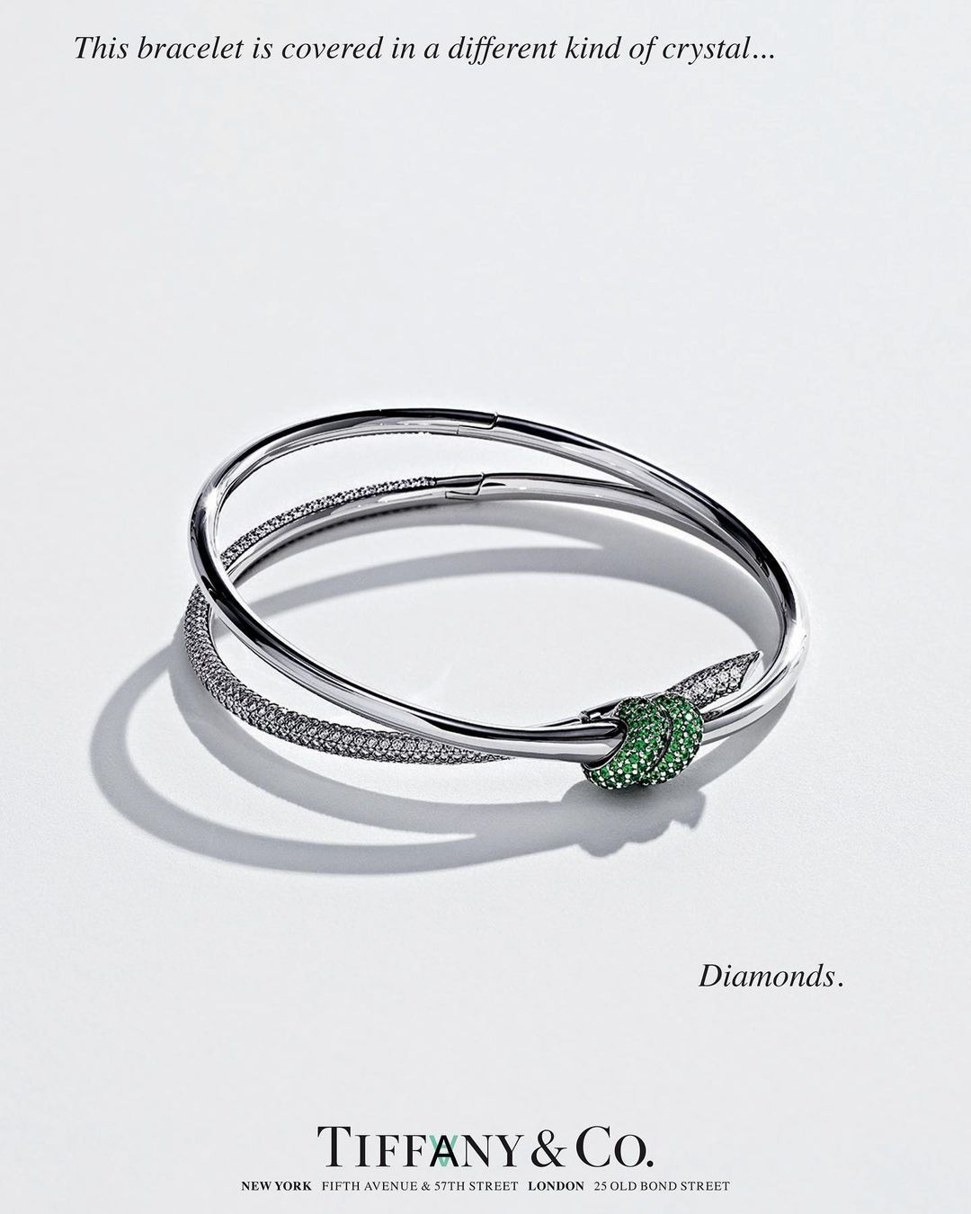 Silver bracelet with a green jeweled knot on a white surface, high-key lighting, Tiffany & Co. jewelry advertisement, close-up.