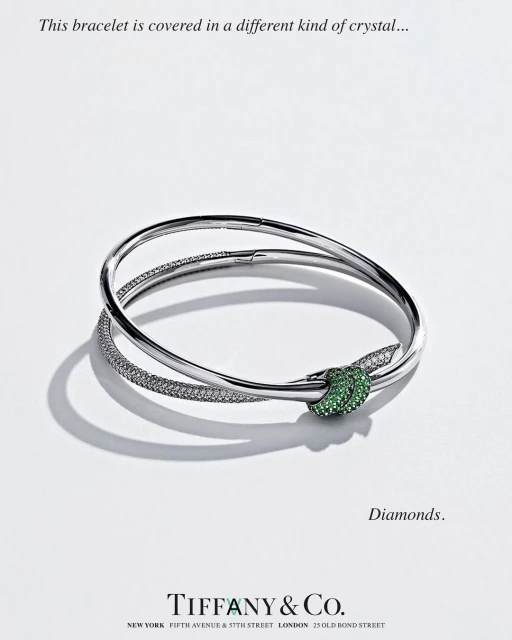 Silver bracelet with a green jeweled knot on a white surface, high-key lighting, Tiffany & Co. jewelry advertisement, close-up.