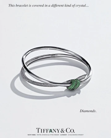 Silver bracelet with a green jeweled knot on a white surface, high-key lighting, Tiffany & Co. jewelry advertisement, close-up.