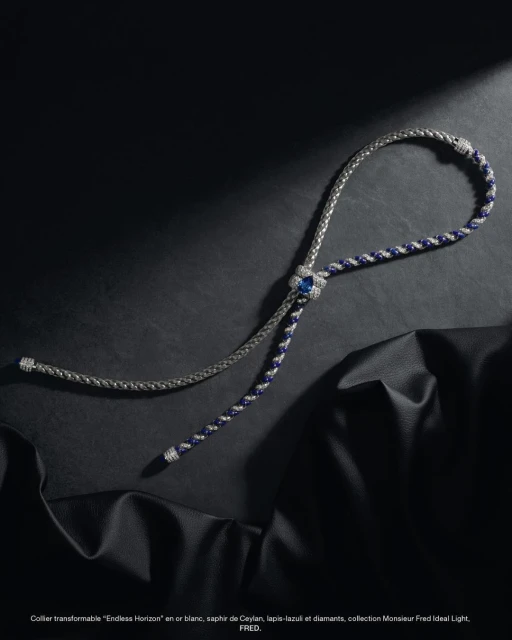 Elegant bolo tie style necklace featuring white gold, sapphires, lapis lazuli, and diamonds, set against a draped black leather surface.