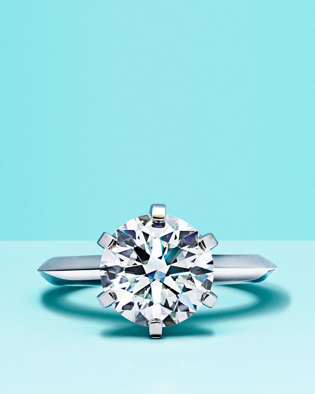 Close-up of a solitaire diamond engagement ring with a platinum band on a light blue background, showcasing its sparkle and clarity.