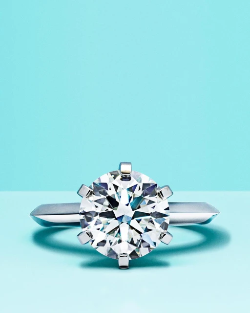 Close-up of a solitaire diamond engagement ring with a platinum band on a light blue background, showcasing its sparkle and clarity.