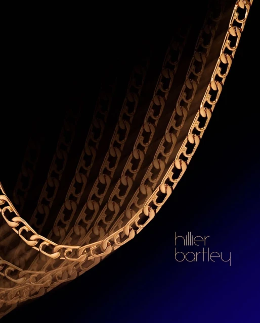 Gold chain necklace against a gradient black-to-blue background with designer Hillier Bartley logo, product photography for fashion.