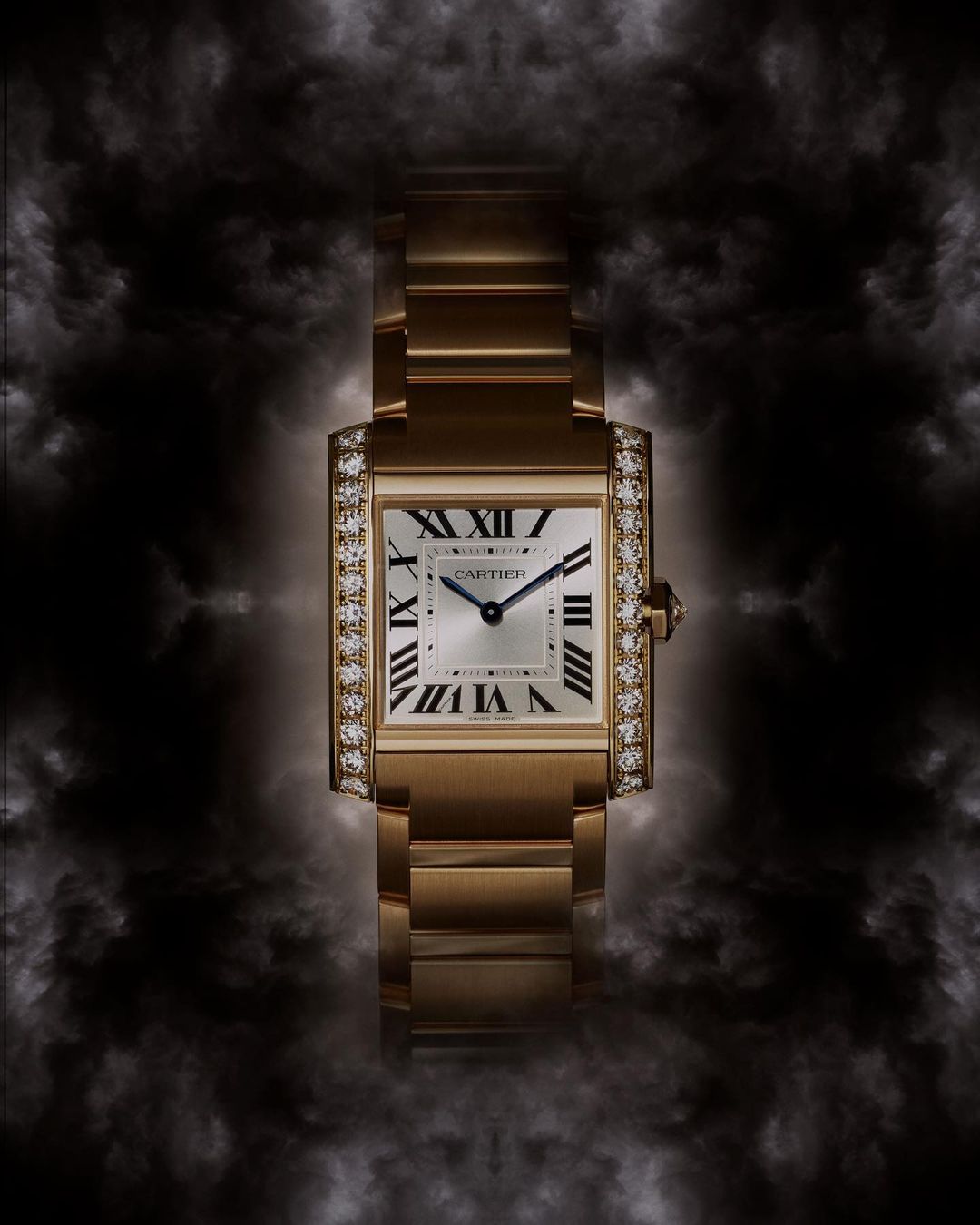 Luxury gold Cartier Tank watch with diamond bezel, set against a dark, smoky background that highlights the watch's details and elegance.