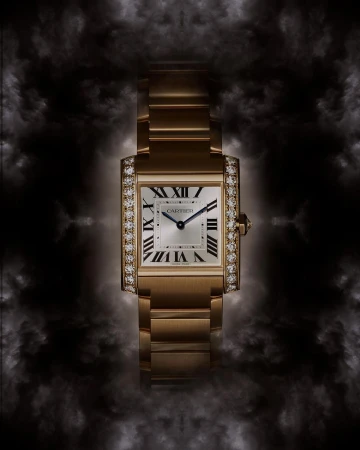 Luxury gold Cartier Tank watch with diamond bezel, set against a dark, smoky background that highlights the watch's details and elegance.