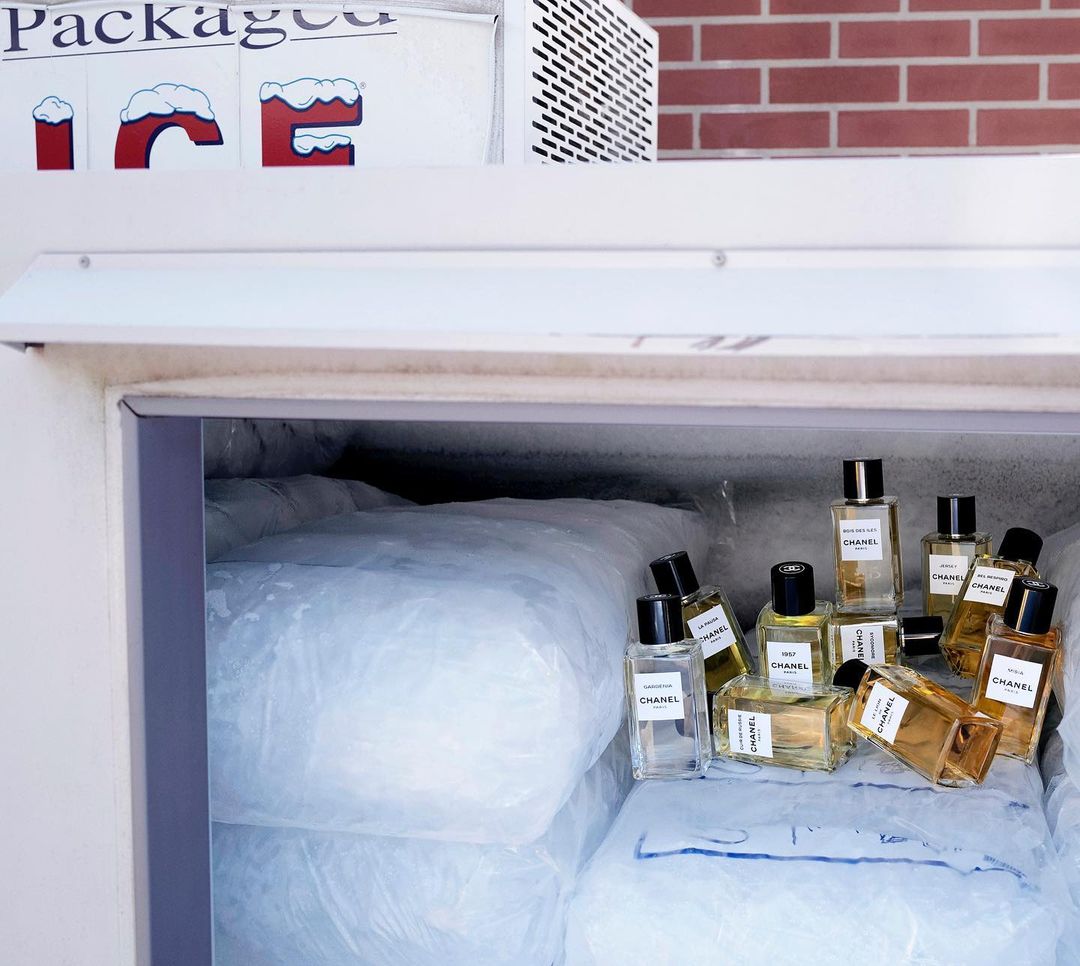 Chanel perfume bottles are displayed amongst bags of ice in a white freezer with a brick background. Beauty and fragrance concept.