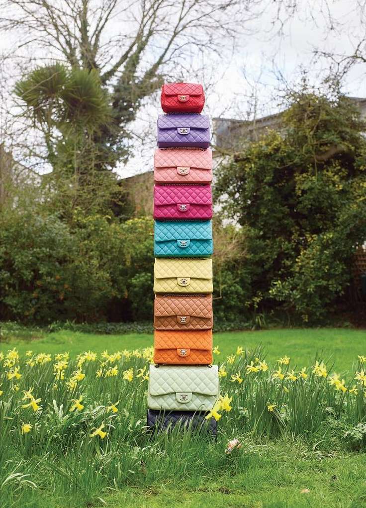 Tower of colorful quilted handbags stacked on each other in a grassy field with yellow flowers. Fashion accessories still life.
