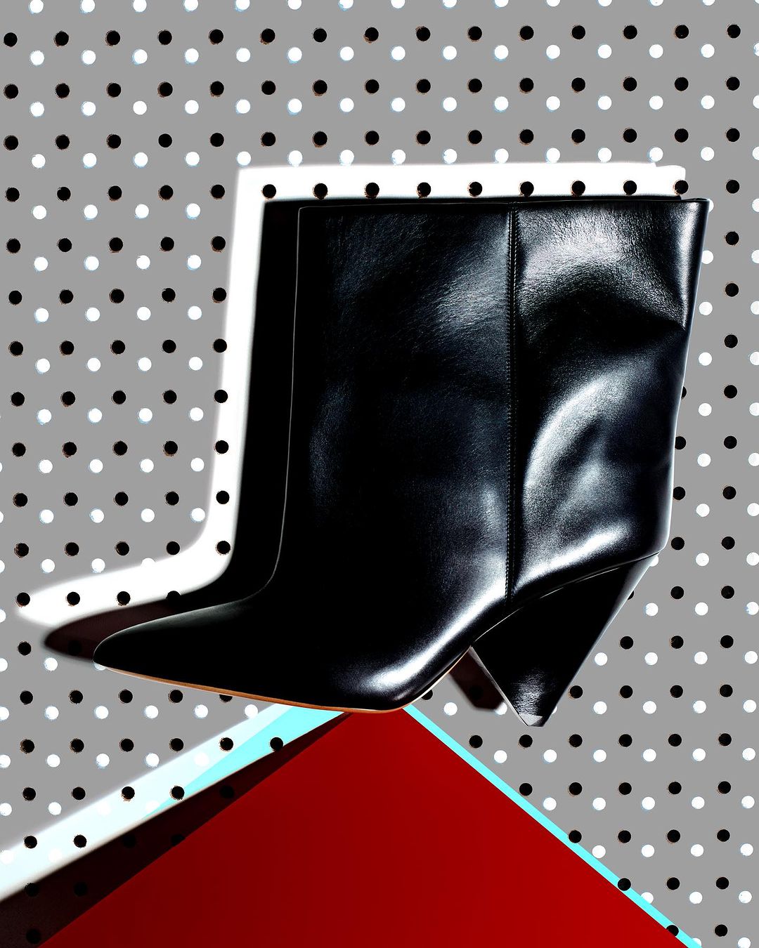 Fashionable black leather ankle boots with pointed toe on a gray polka dot background, elevated by a red and teal geometric platform.