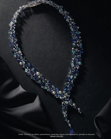 Elegant blue gemstone necklace made of tanzanite, sapphires, and pearls, displayed on a draped black fabric background in a jewelry advertisement.